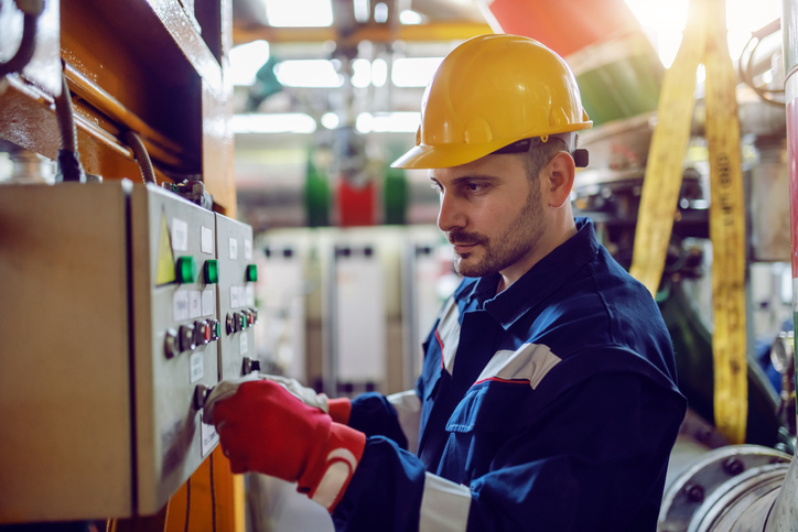 Side view of caucasian energy plant worker in working clothes and with helmet on head turning on switch. refineries maintenance services