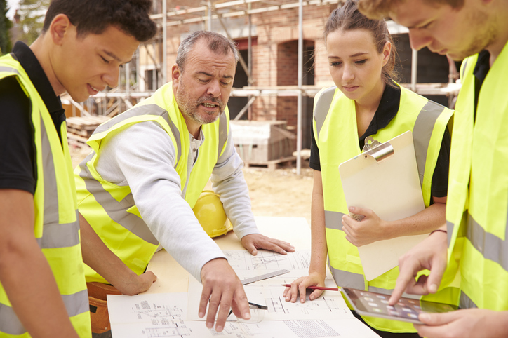 Builder On Building Site Discussing Work With Apprentice Construction Industry Maintenance Services